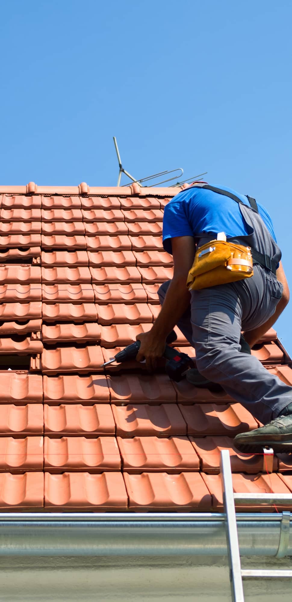 Dachdecker bei der Dachreparatur – verlegt Dachziegel mit Akku-Bohrschrauber auf einem Steildach